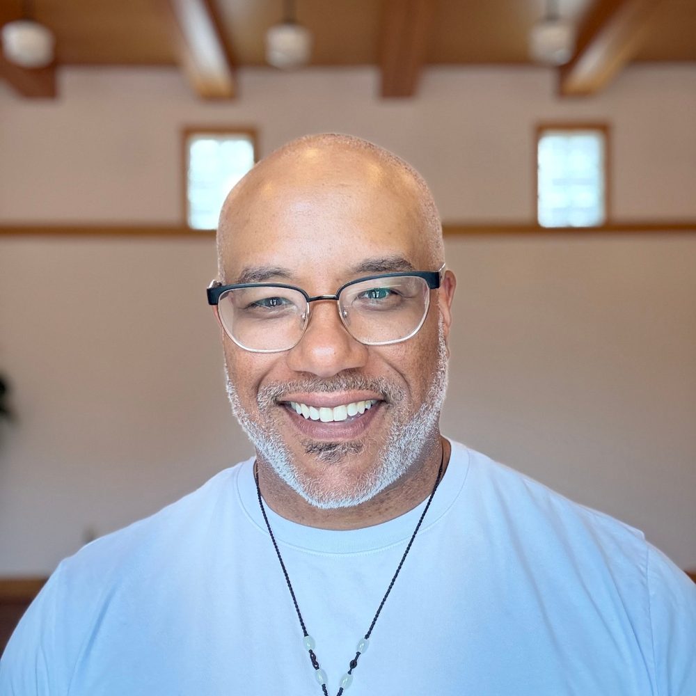 Dr. Stephen Thompson smiling, in glasses and a light blue shirt, in a room with wooden beams